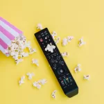 Imagem de um saco de pipoca espalhada e controle de TV