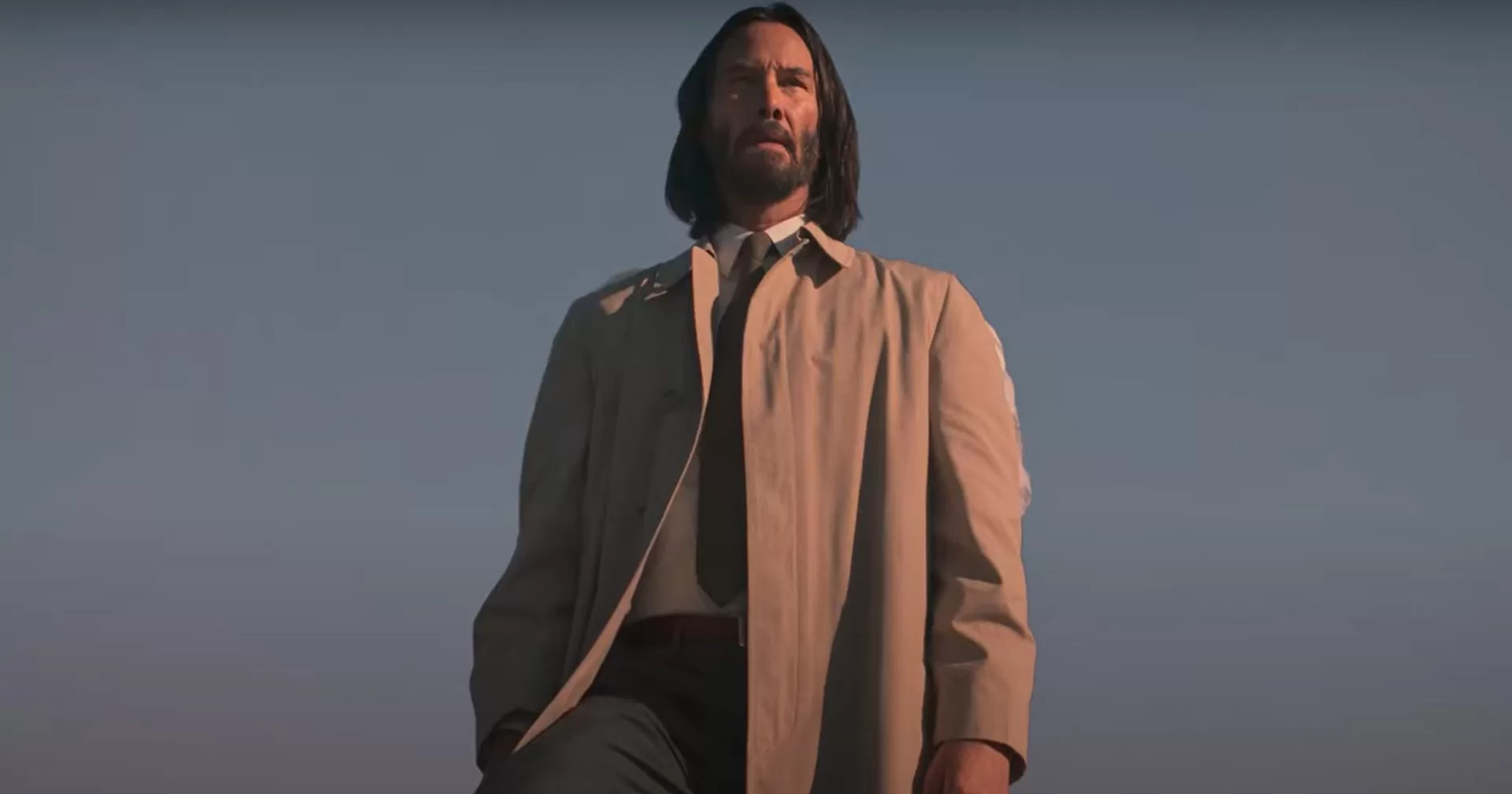 Keanu Reeves em pose contemplativa no filme "Quando o Céu se Engana", vestindo sobretudo claro sob o céu azul