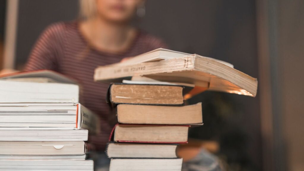 Pilha de livros sendo estudados por uma mulher