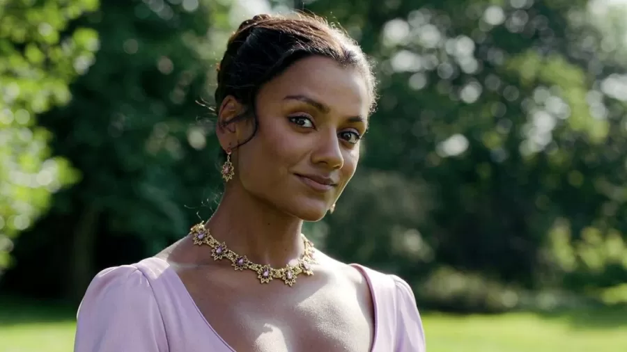 Simone Ashley com vestido lilás e joias florais em cenário natural, atriz é destaque da série Bridgerton
