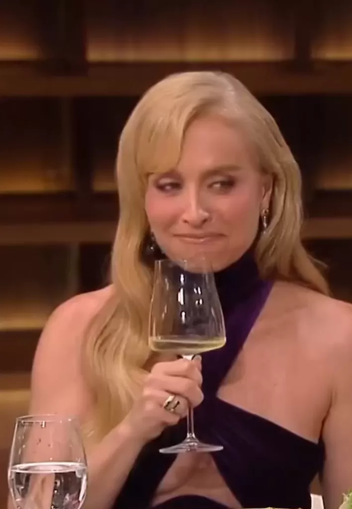 Angélica segurando taça de vinho e olhando para o lado